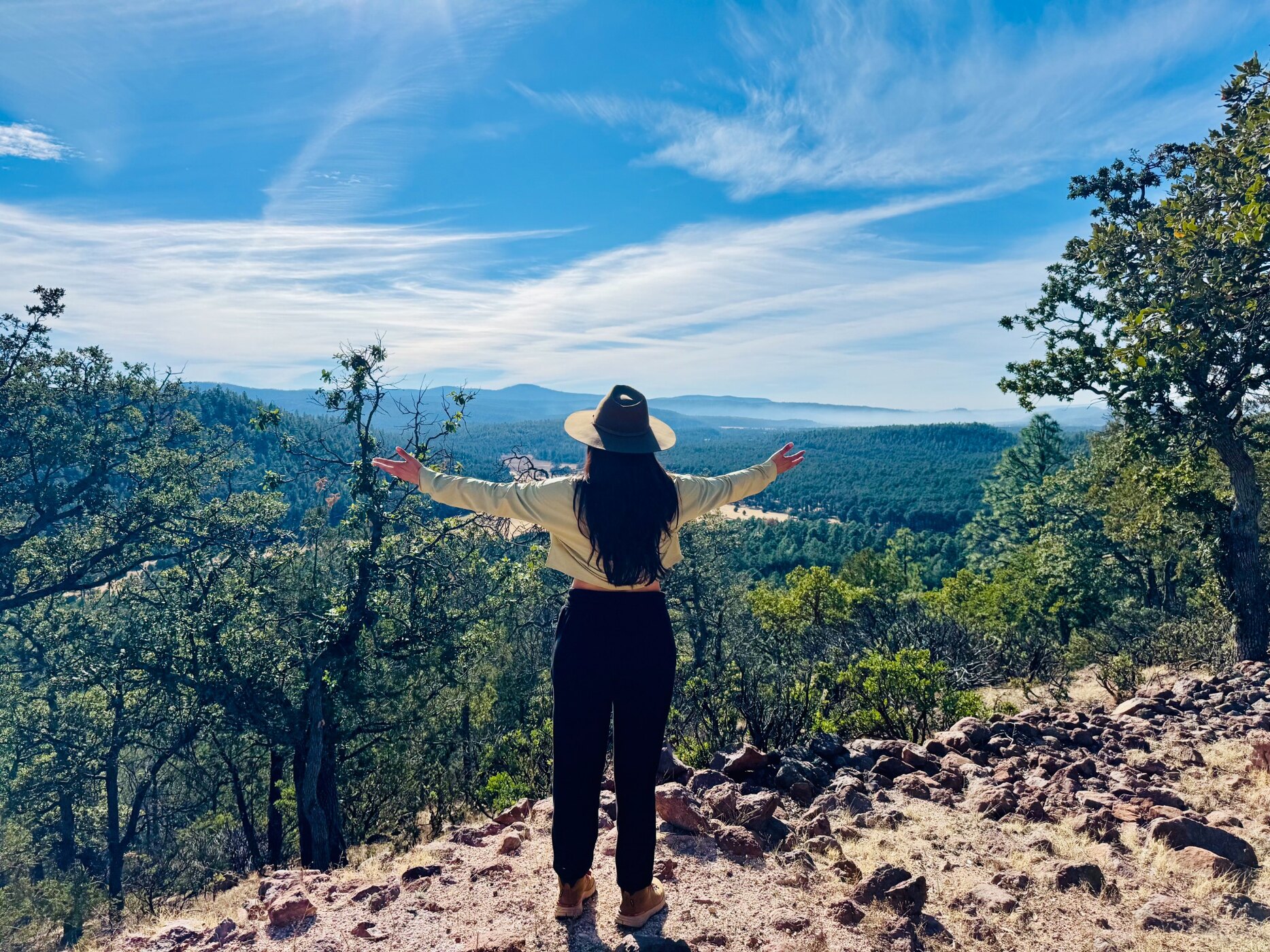 Isis de espaldas, con los brazos abiertos frente al bosque de la Sierra de Chihuahua
