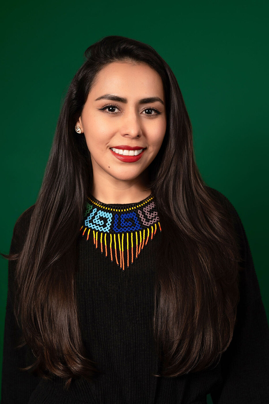 Retrato profesional de Isis J. Silva con collar de chaquira y fondo verde